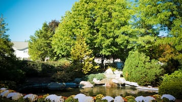 A serene garden with a pond, lush greenery, and a white building in the background.