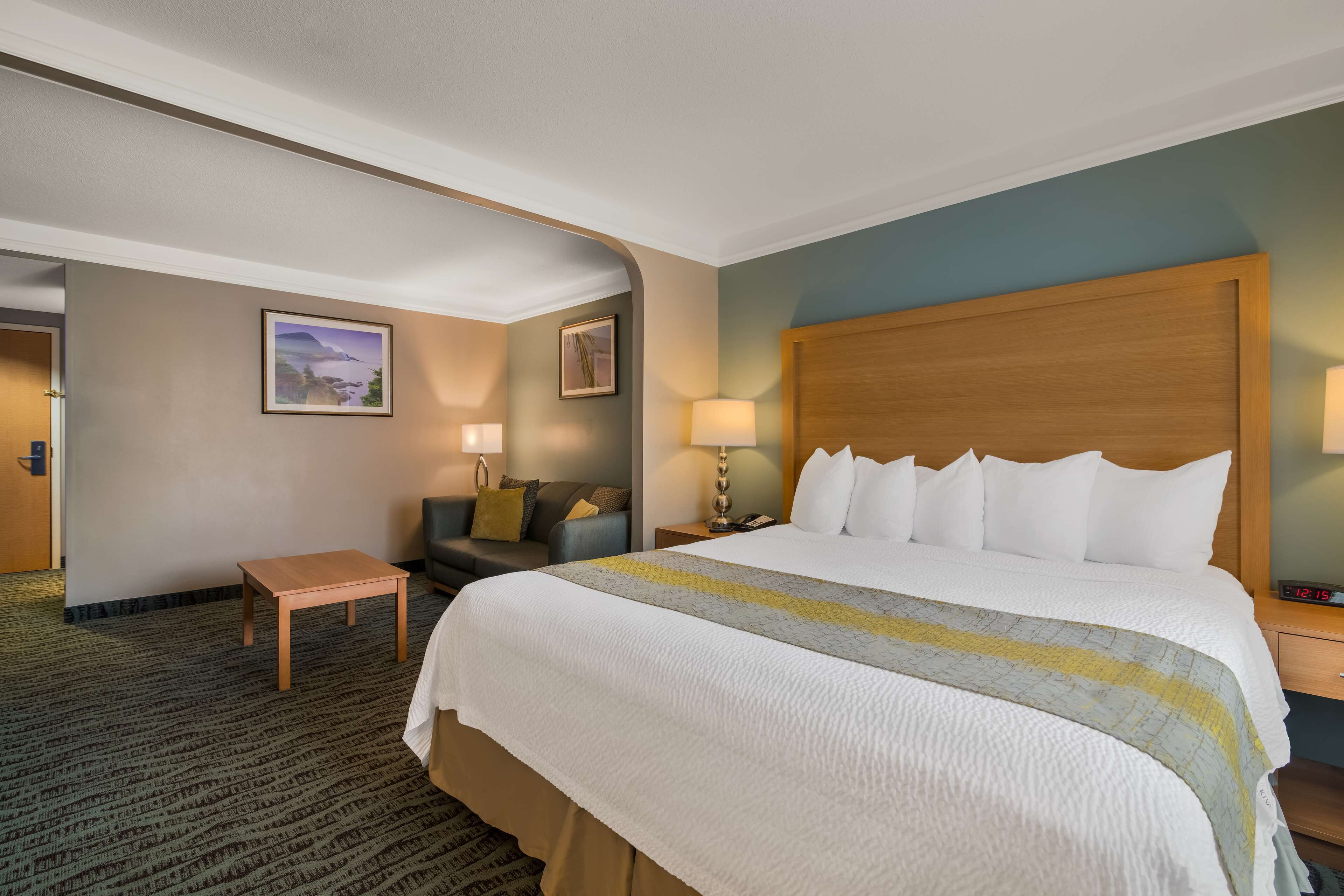 A hotel room with a large bed, a small table, a sofa, and two lamps.