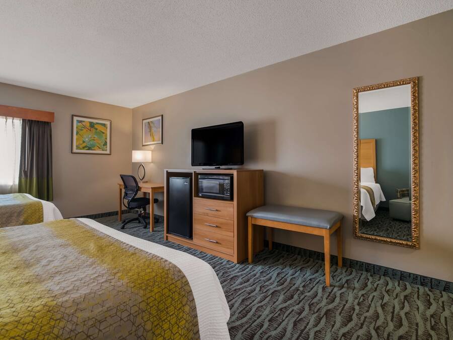 A hotel room with two beds, a desk with a computer, a television, a mirror, and a small cabinet.