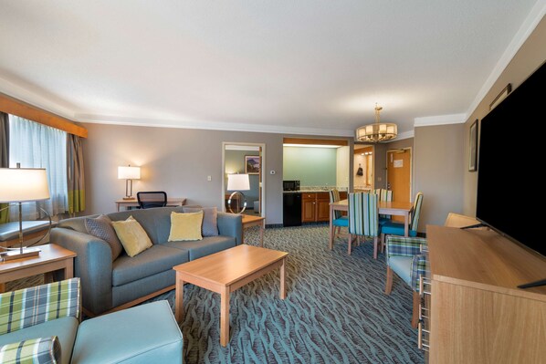 A hotel room with a living area, a dining table, a sofa, a coffee table, and a TV.
