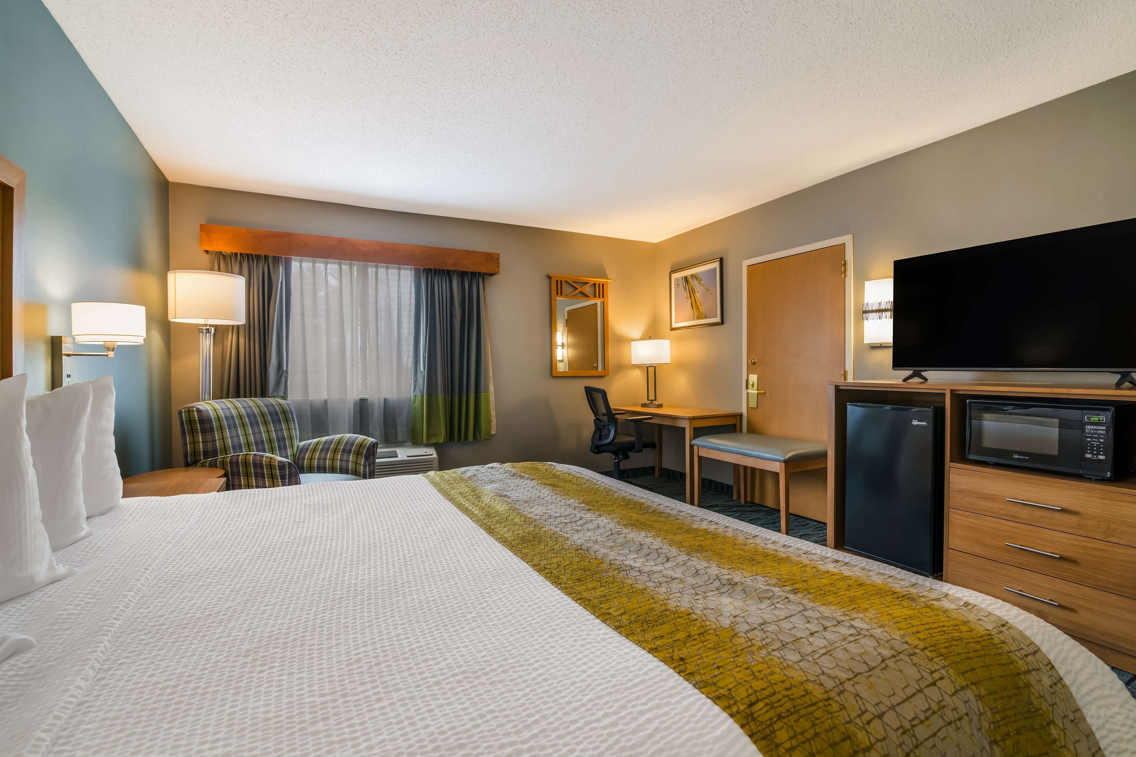 Habitación de hotel con una cama grande, un escritorio, una silla, un televisor y un refrigerador.