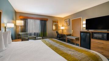 A hotel room with a large bed, a desk, a chair, a television, and a refrigerator.