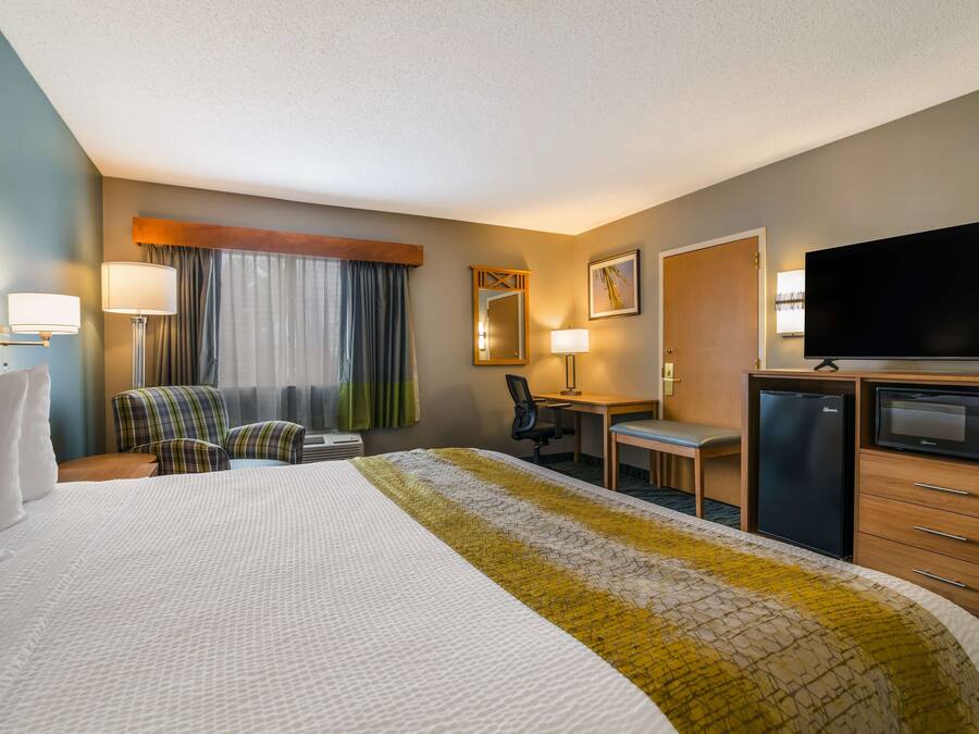 A hotel room with a large bed, a desk, a chair, a television, and a refrigerator.