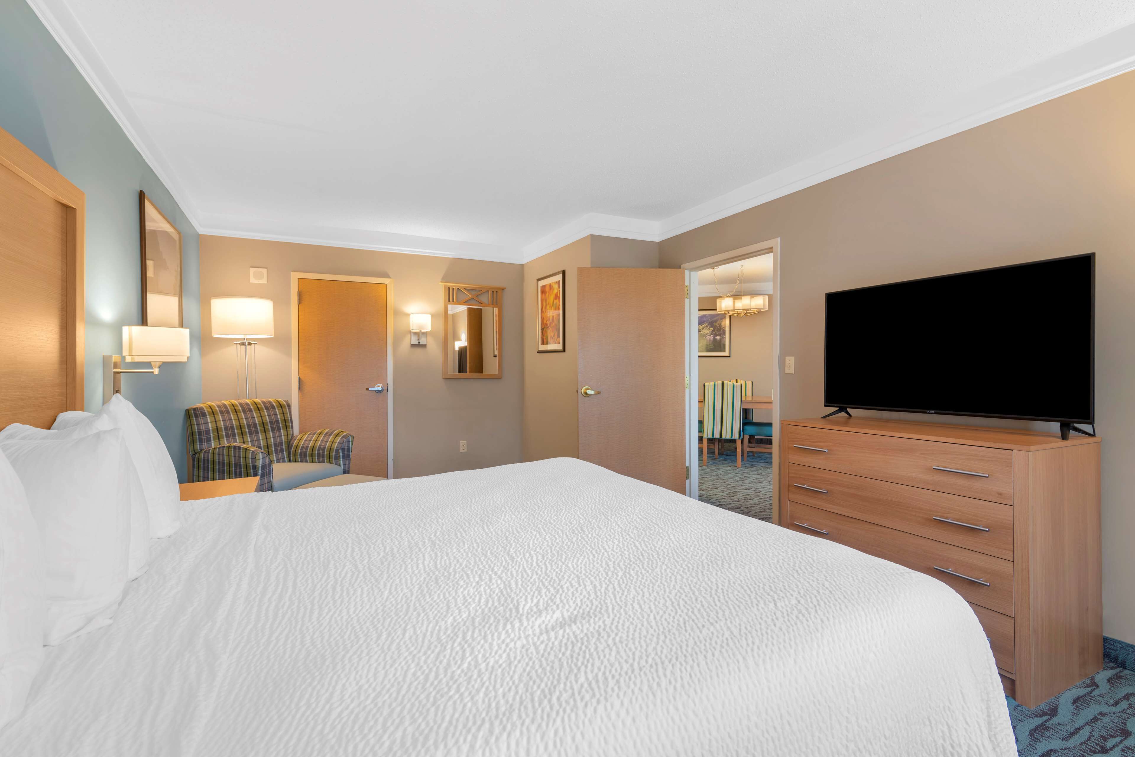 Habitación de hotel con una cama grande, televisor, cómoda, silla y escritorio con lámpara.