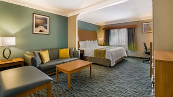 A hotel room with a bed, a sofa, a coffee table, a desk, and a lamp.