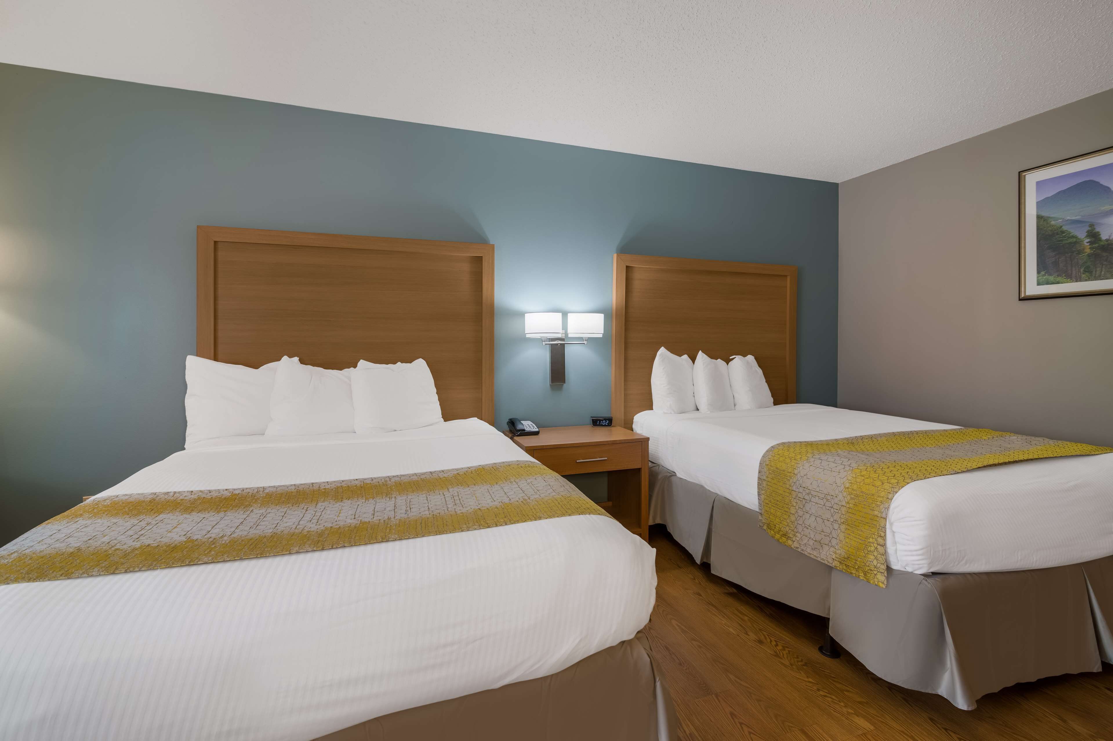 A hotel room with two beds, a nightstand with a lamp, and a painting on the wall.