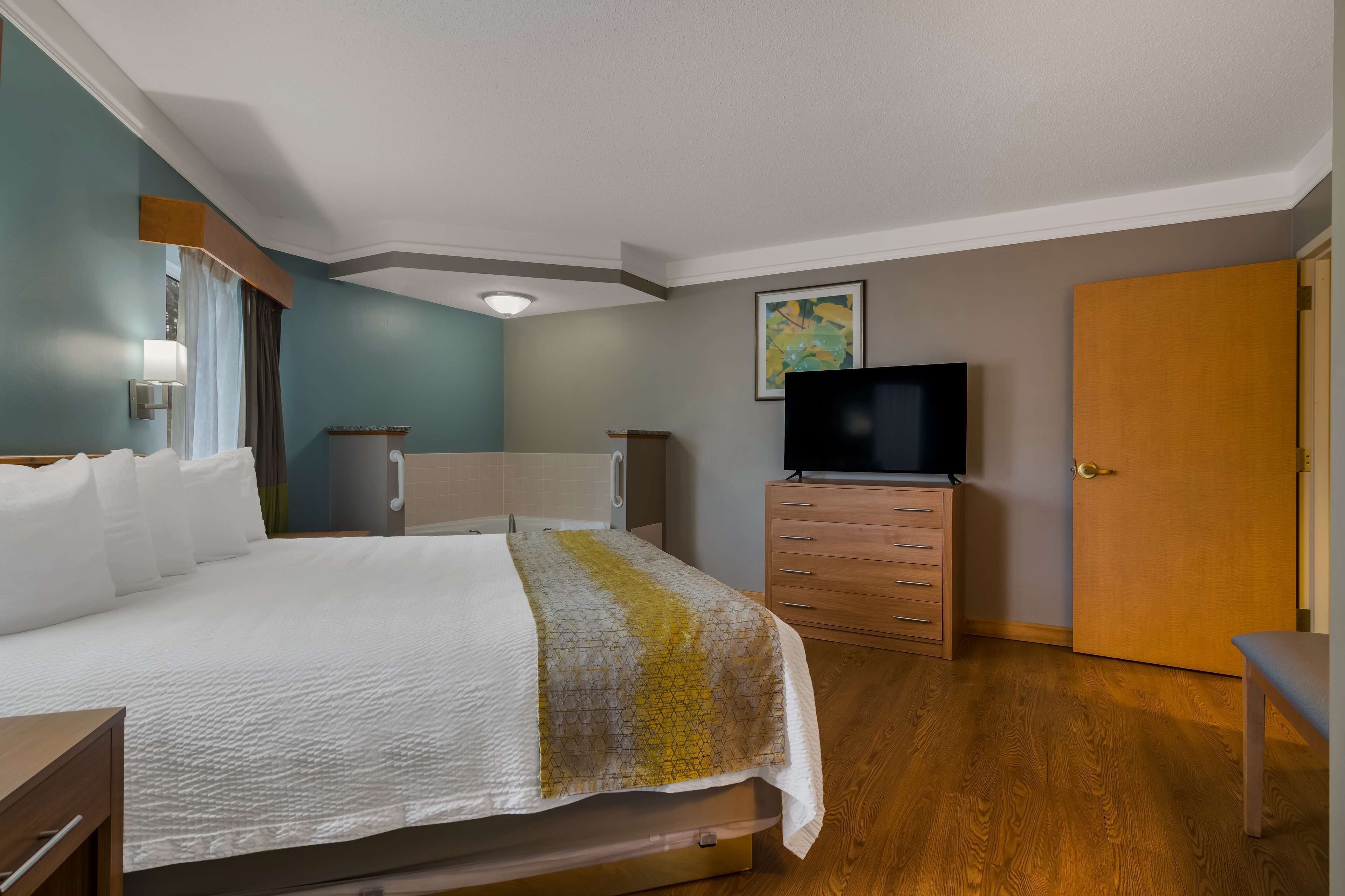 A hotel room with a bed, a TV, a wooden dresser, and a door.