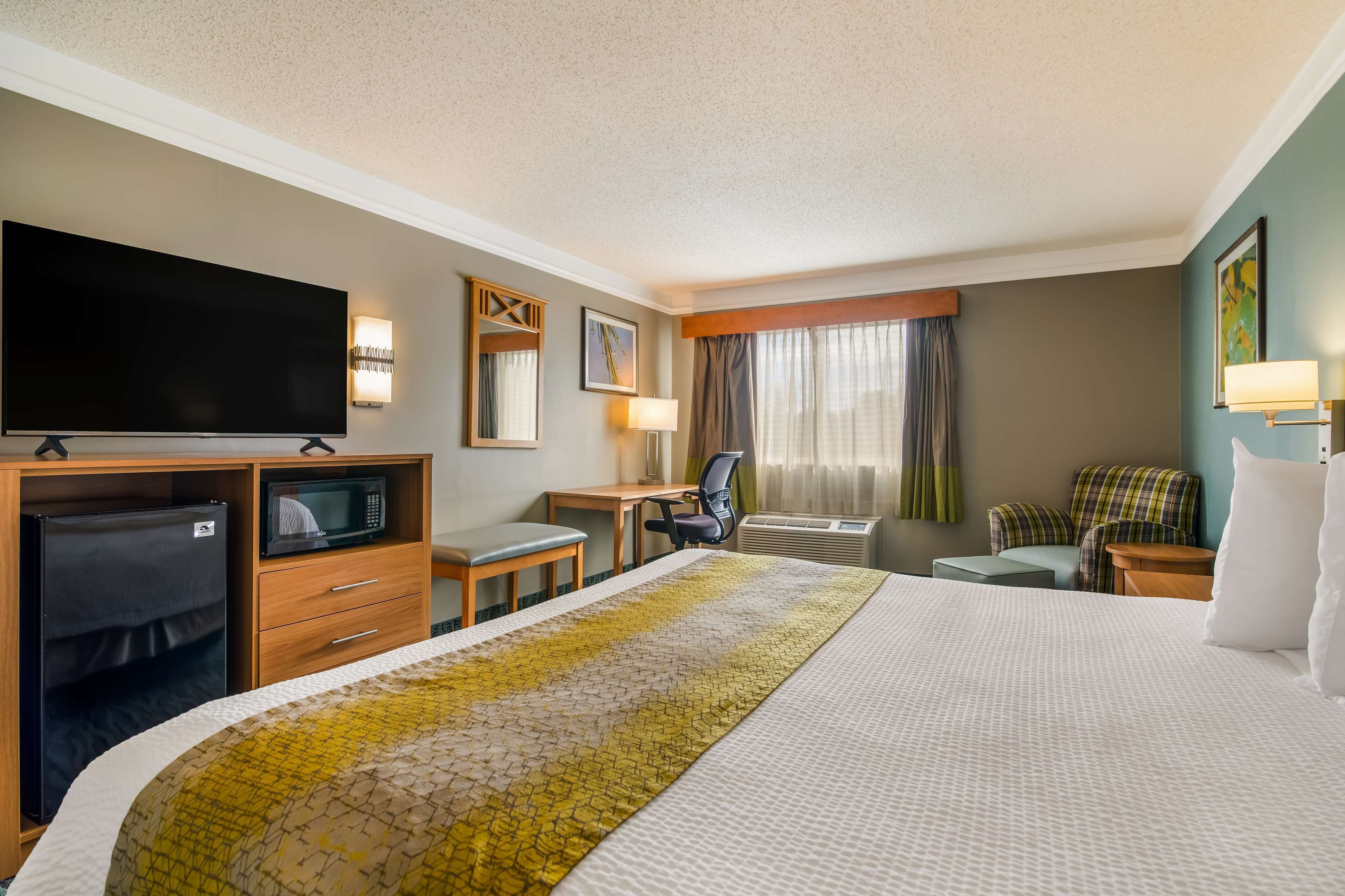 A hotel room with a large bed, a desk with a chair, a television, a microwave, and a seating area with a couch and chairs.