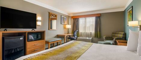 A hotel room with a large bed, a desk with a chair, a television, a microwave, and a seating area with a couch and chairs.