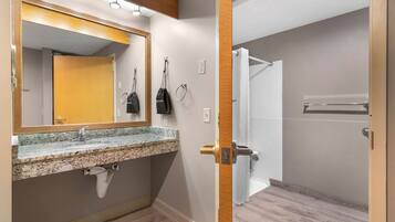 Un baño con lavamanos de granito, espejo, toallero y zona de ducha.