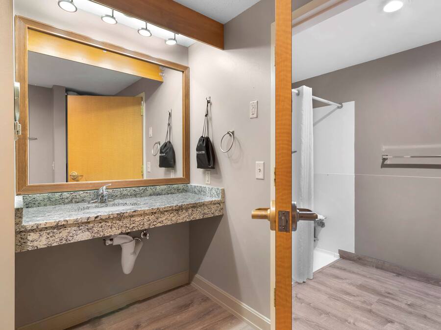 Un baño con lavamanos de granito, espejo, toallero y zona de ducha.
