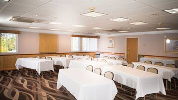 A conference room with multiple tables and chairs, carpeted floor, and ceiling lights.