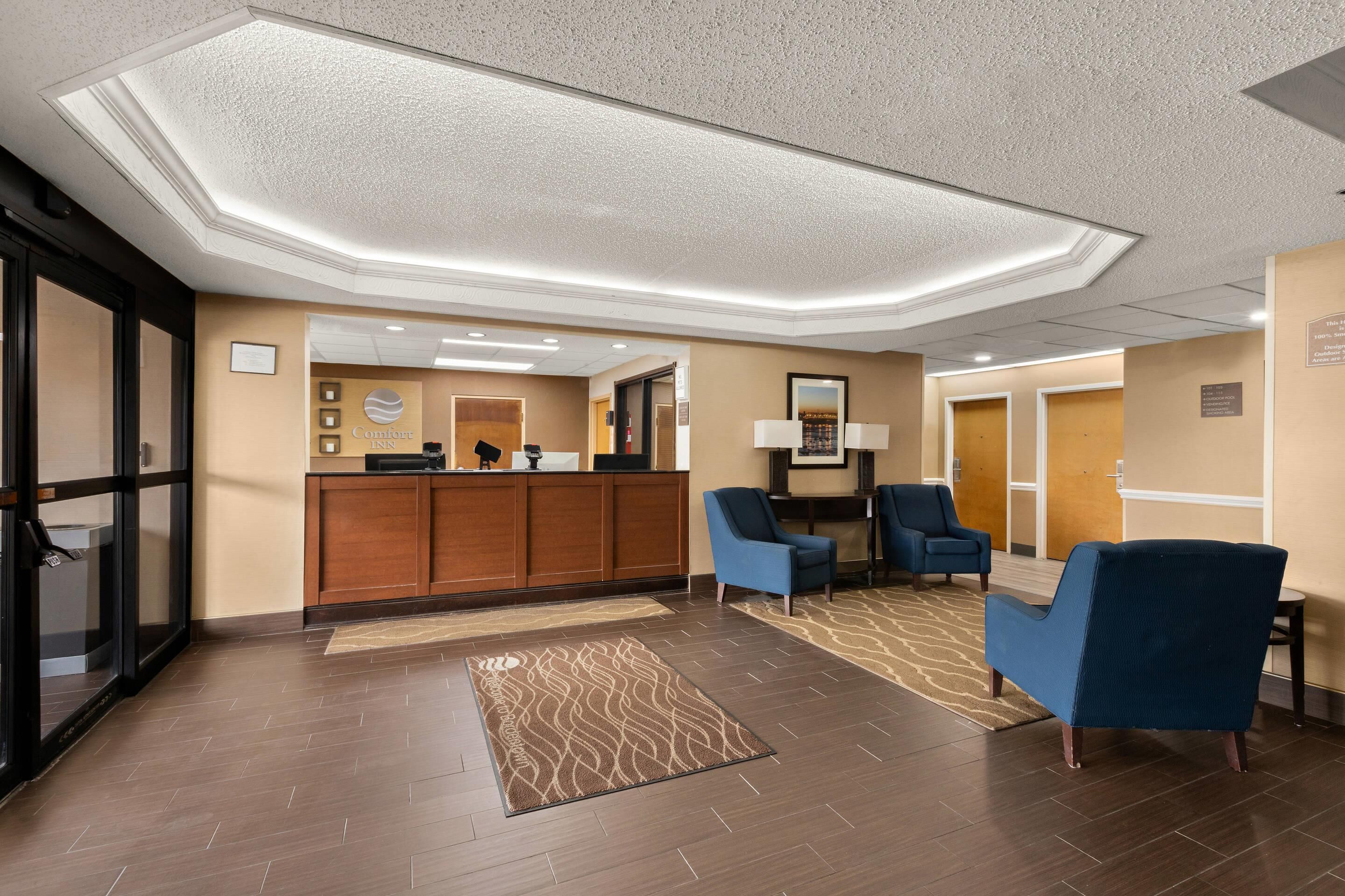 A hotel lobby with a reception desk, blue armchairs, a patterned rug, and a modern ceiling design.