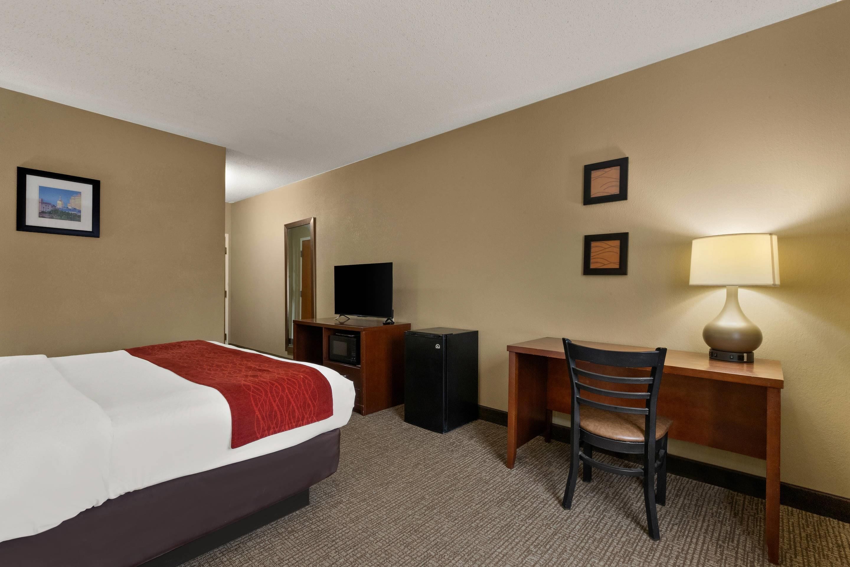 Habitación de hotel con cama, escritorio, silla, televisor, lámpara y cuadros en la pared.