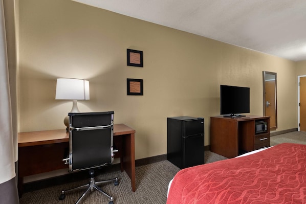 Une chambre d’hôtel équipée d’un lit, d’un bureau, d’une chaise, d’une télévision et d’un réfrigérateur.
