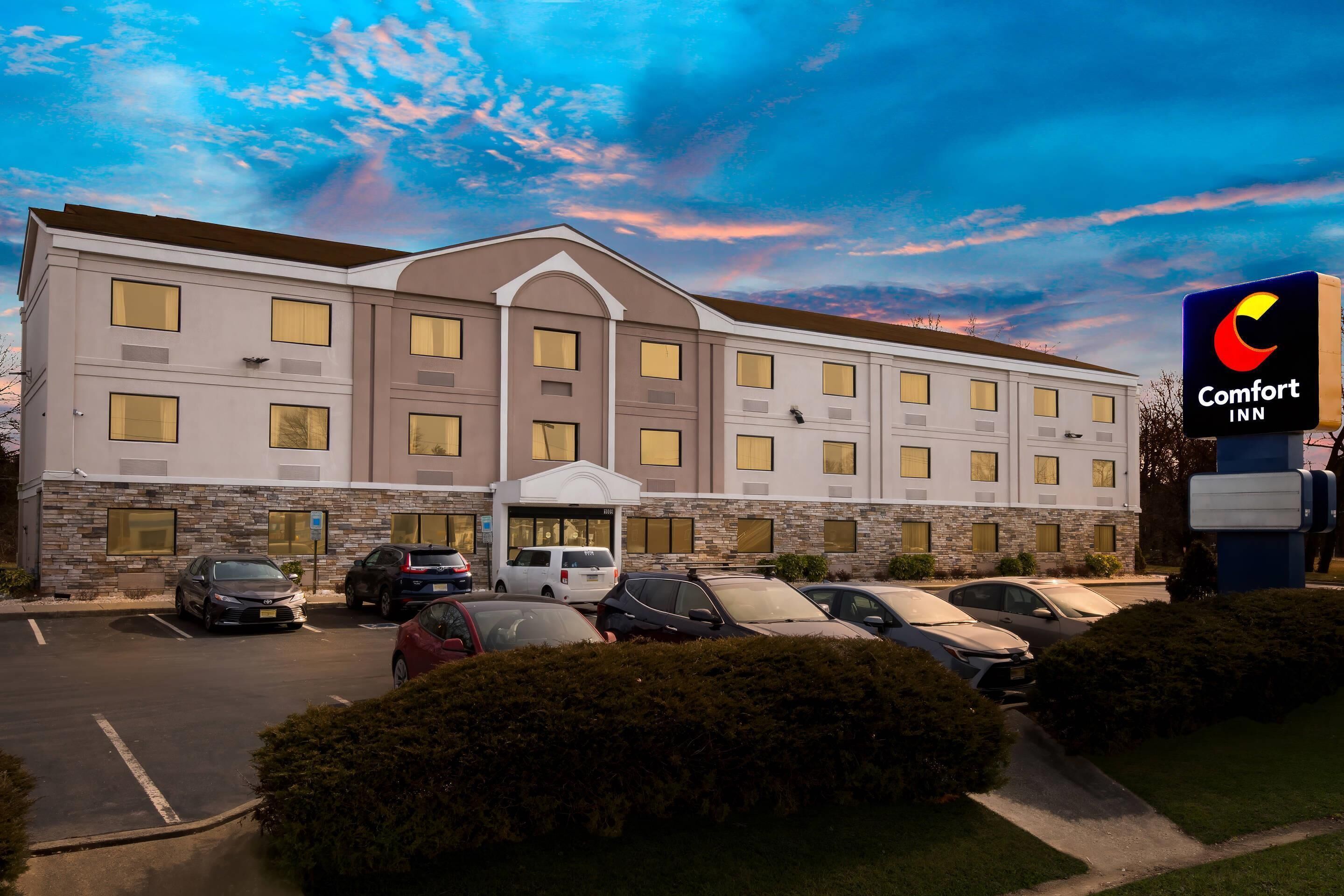 Un hotel Comfort Inn con un estacionamiento, varios autos y cielo despejado con nubes.