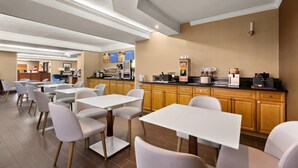 Un comedor moderno con mesas y sillas blancas, armarios de madera y una estación de café.