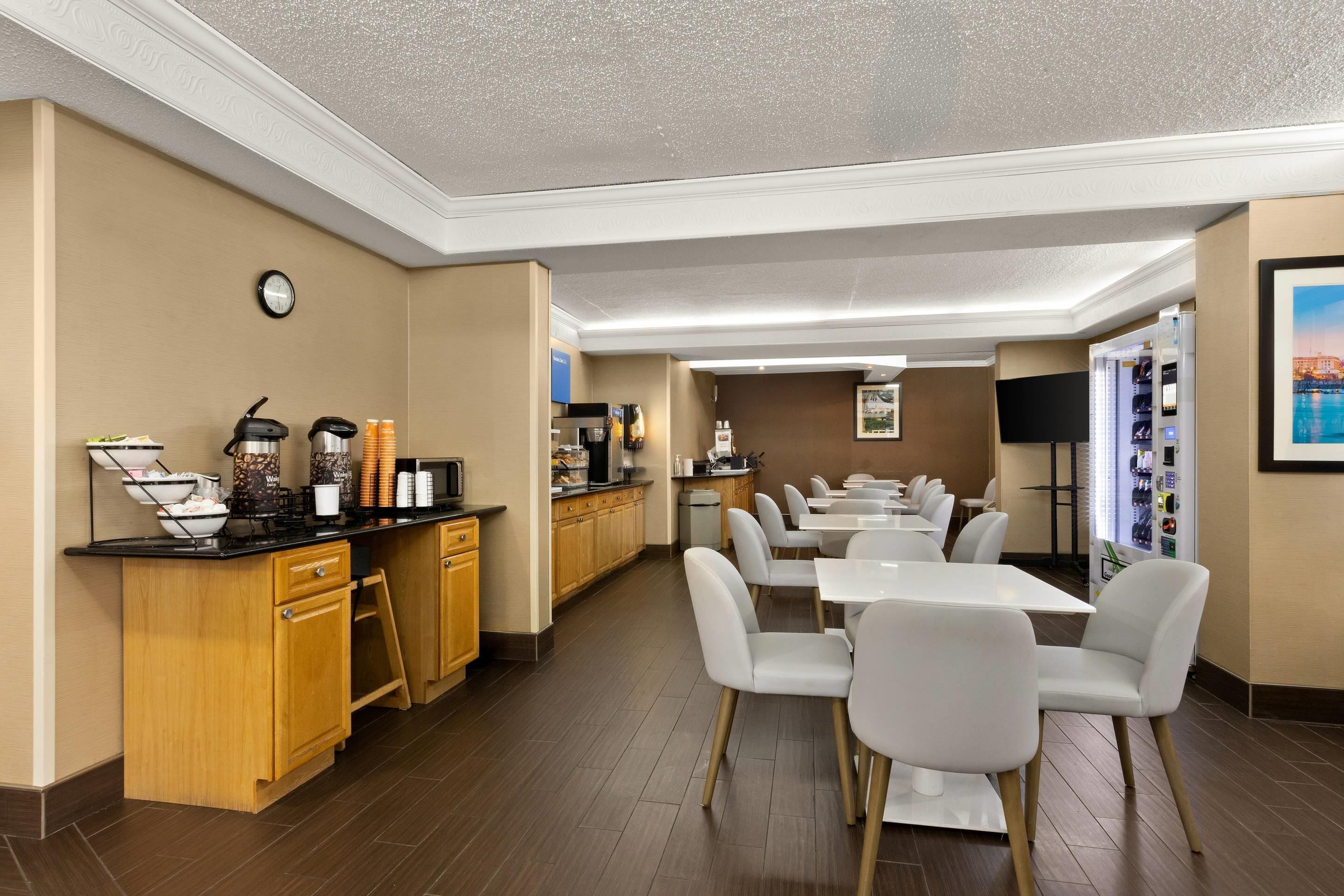A hotel breakfast area with a counter, seating, and a clock on the wall.