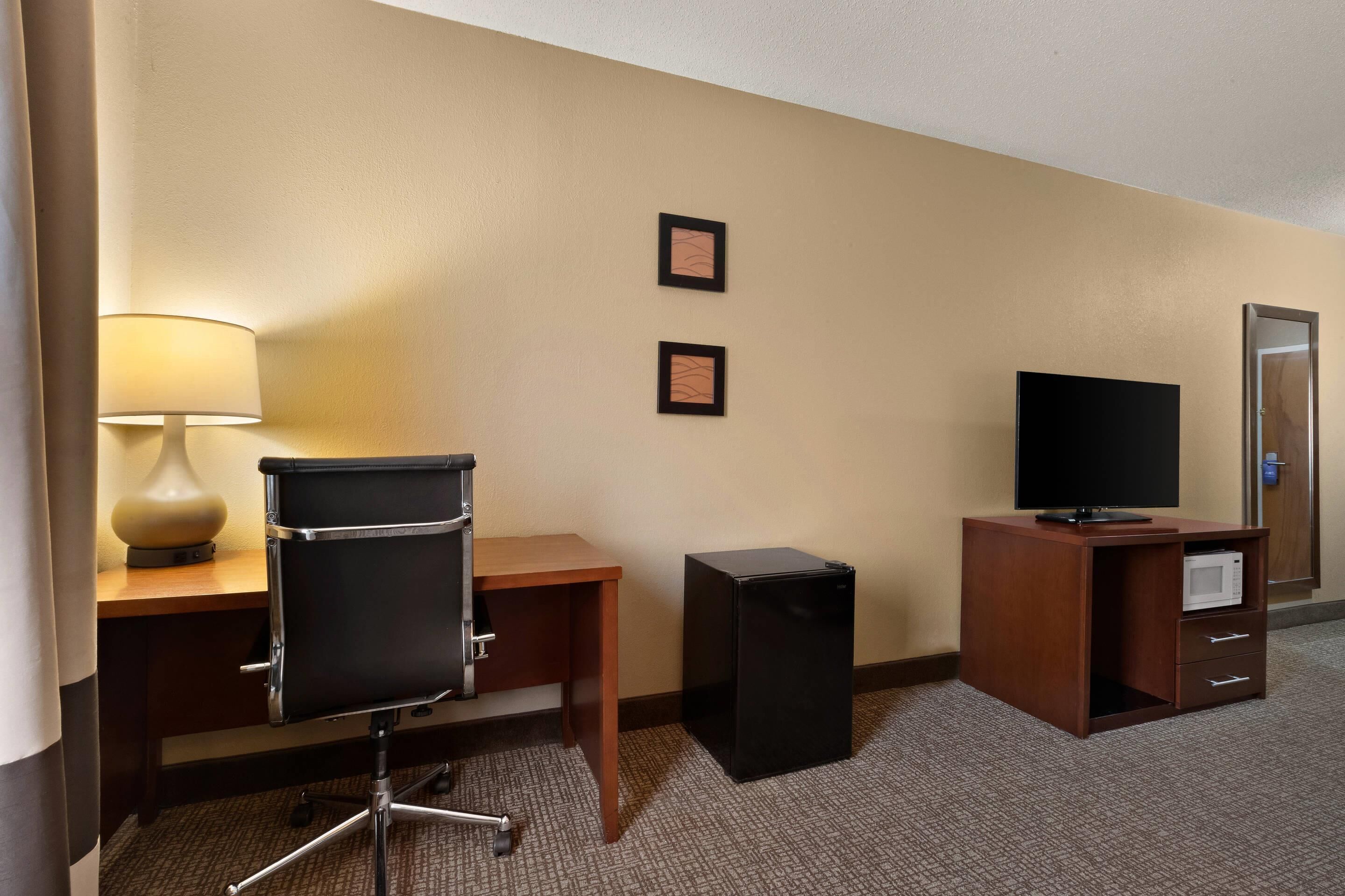 Une chambre d’hôtel équipée d’un bureau, d’une chaise, d’une lampe, d’une télévision, d’un mini-réfrigérateur et d’un four à micro-ondes.
