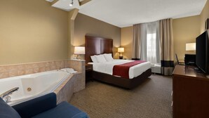 Habitación de hotel con una cama grande, baño independiente con bañera, escritorio con televisor y lámpara de escritorio.