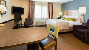 Een hotelkamer met een bed, een bureau met stoel, een televisie en een raam met gordijnen.
