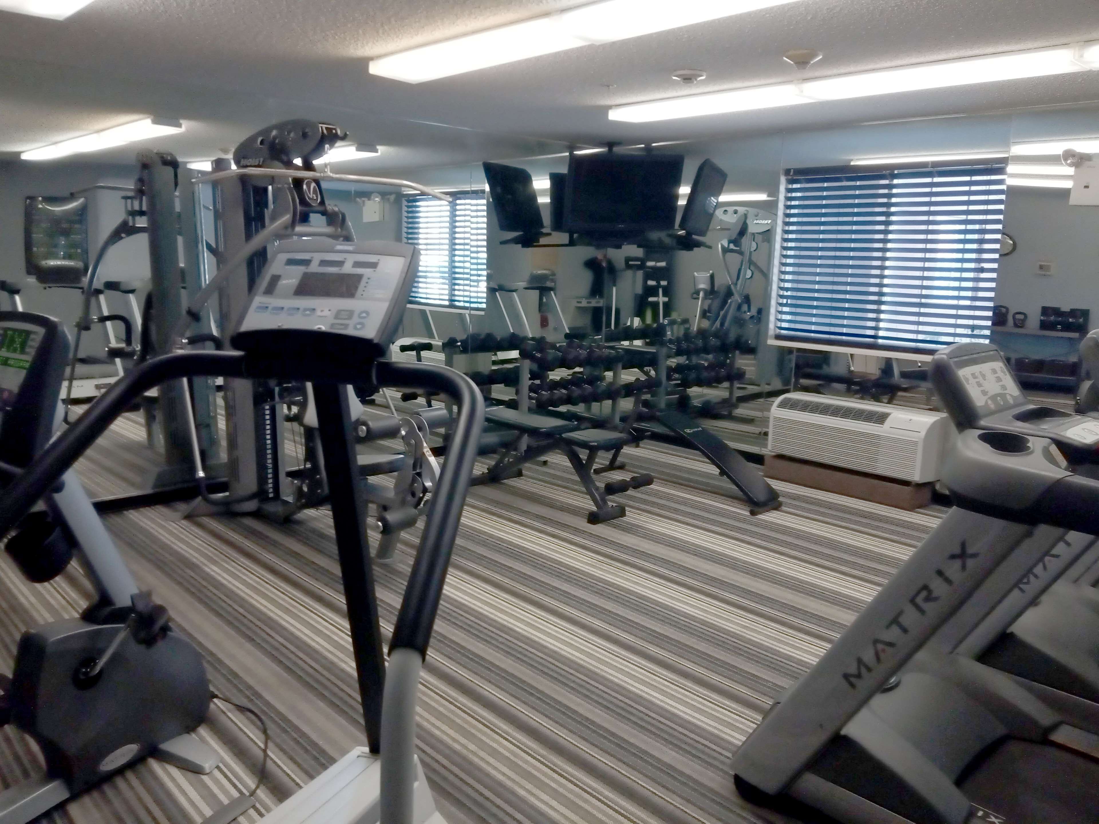 Une salle de sport équipée de divers appareils d’exercice, notamment des tapis de course, des appareils de musculation et des haltères.