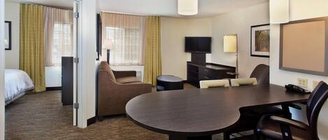 A hotel room with a bed, a seating area with a table and chairs, a television, and a lamp.