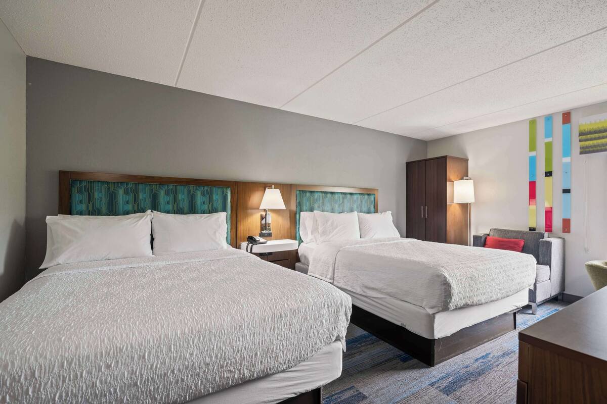 A hotel room with two beds, a desk, a chair, a lamp, and a wardrobe.