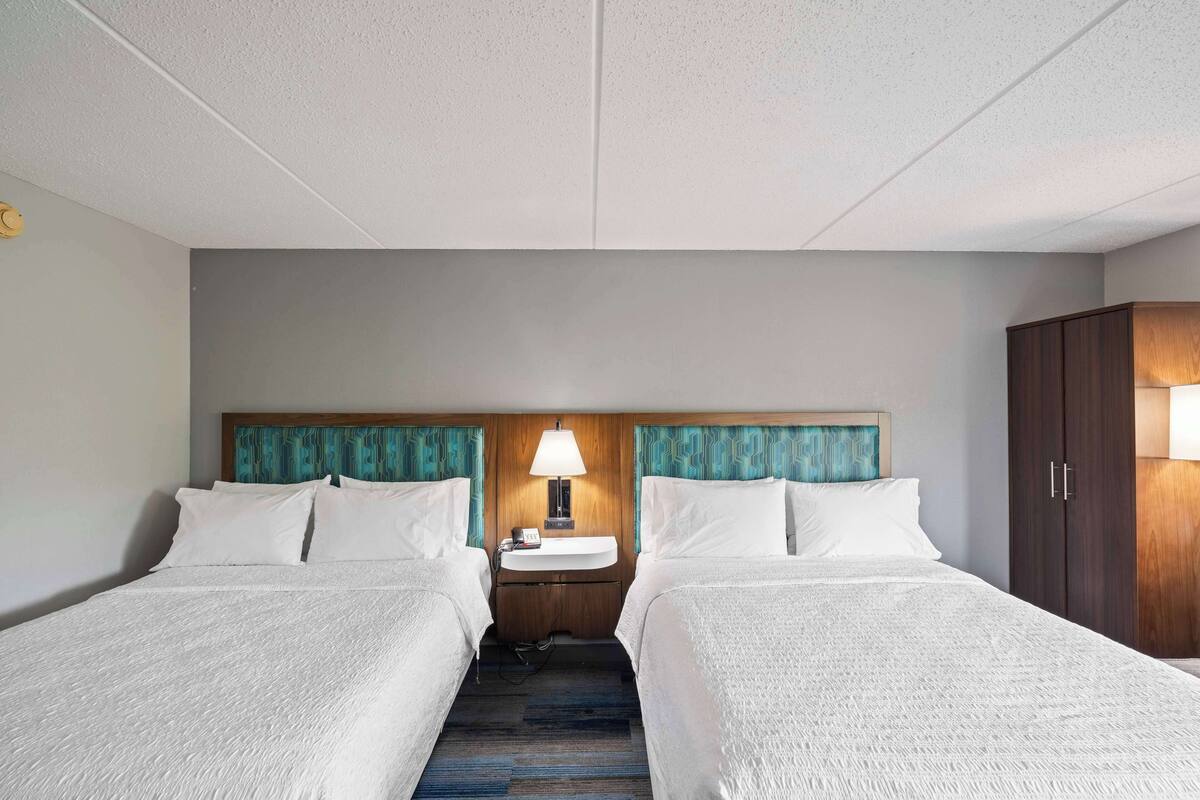 A hotel room with two beds, a nightstand, a sink, and a wardrobe.