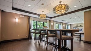 A spacious hotel lobby with a bar area, wooden flooring, and large windows offering a view of greenery outside. - Hampton Inn Ridgefield Park (Ridgefield Park)