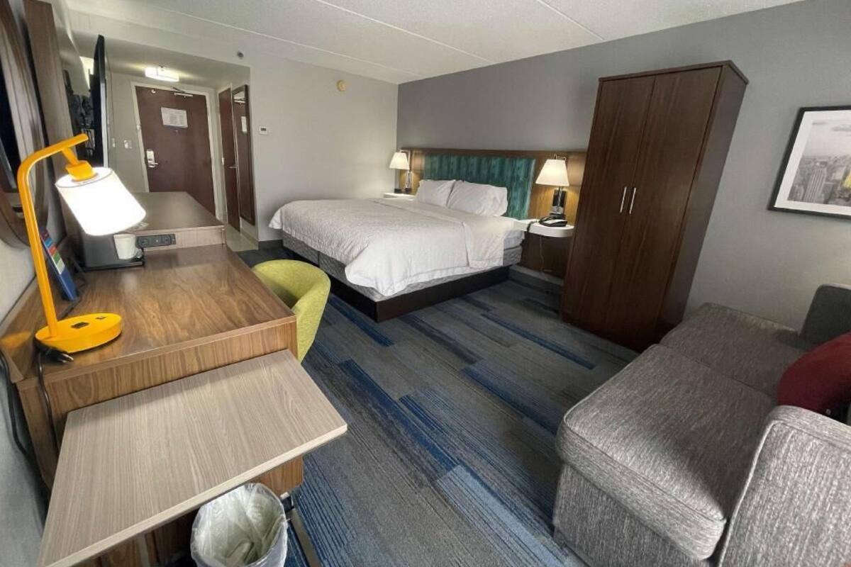 Habitación de hotel con cama, escritorio con lámpara, silla, armario y una mesita.