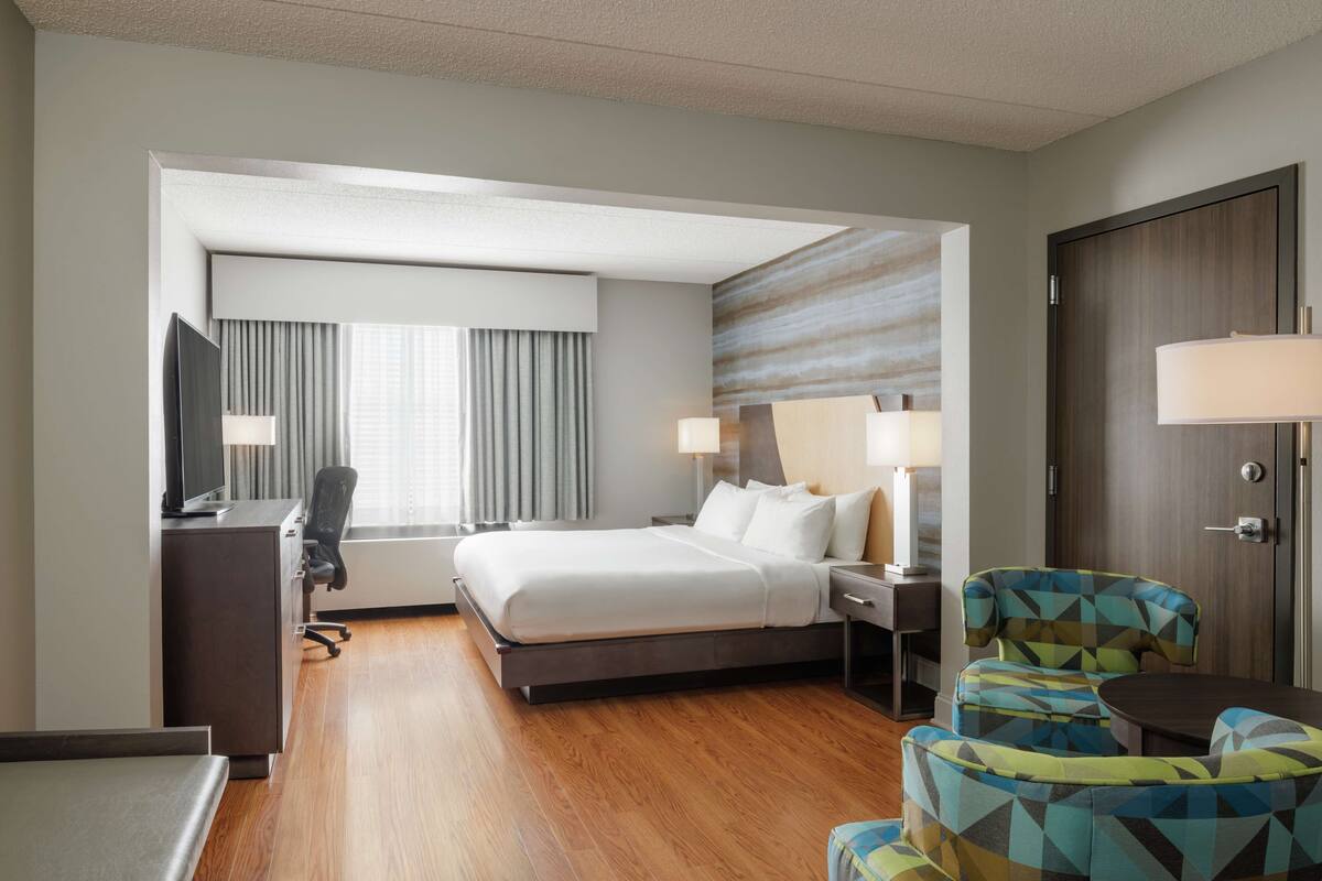 A hotel room with a bed, desk, chair, and a TV.
