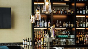A bar area with a marble countertop, hanging pendant lights, and a variety of bottles and glasses on shelves. - Hotel Trilogy Albany Airport, Tapestry Collection by Hilton (Latham)