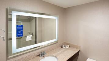 A bathroom with a large mirror, a sink, a toilet, and a shower.