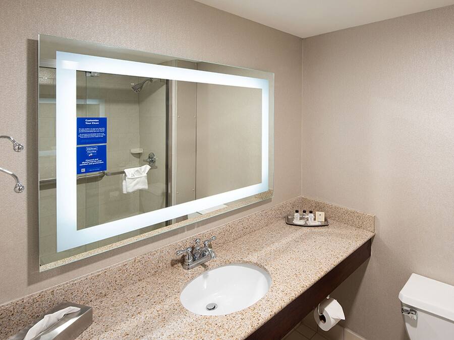 A bathroom with a large mirror, a sink, a toilet, and a shower.