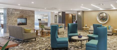 A modern lobby with teal armchairs, a grey sofa, and a marble-patterned carpet.