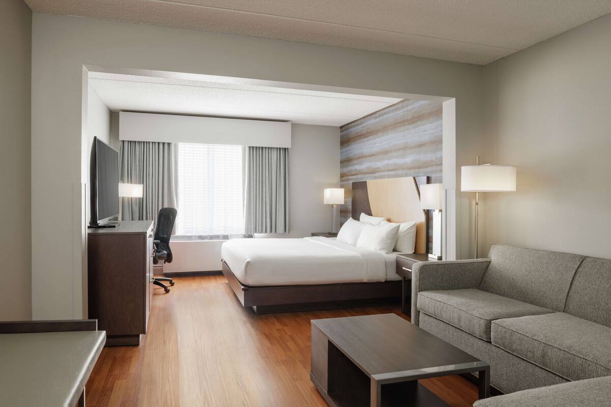 A modern hotel room with a large bed, a desk, a sofa, and a TV.