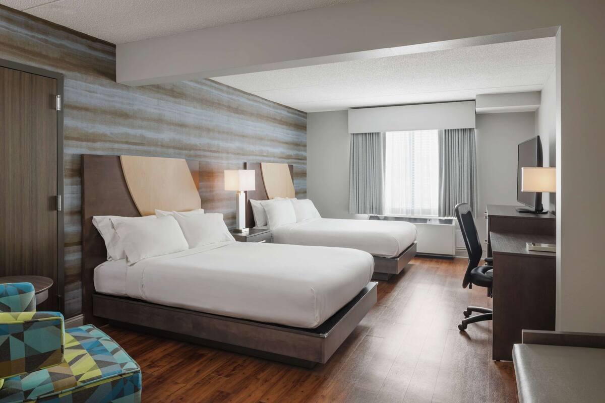 A hotel room with two beds, a desk, a chair, a TV, and a window with curtains.