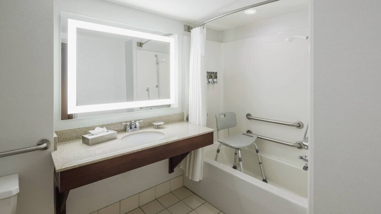 A modern bathroom with a large mirror, a sink, a shower, and a grab bar.