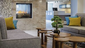 A modern lobby with a fireplace, sofas, and round wooden tables. - Hotel Trilogy Albany Airport, Tapestry Collection by Hilton (Latham)