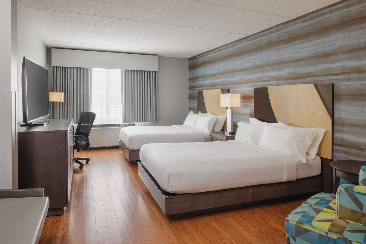 A hotel room with two beds, a desk with a TV, a chair, and a small table.