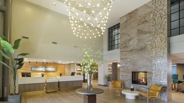 A modern hotel lobby with a reception desk, seating area, and a fireplace. - Hotel Trilogy Albany Airport, Tapestry Collection by Hilton (Latham)