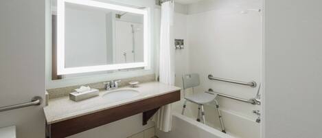 A modern bathroom with a double sink, a large mirror, a shower, and a wheelchair-accessible chair.