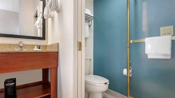 A bathroom with a blue wall, a white toilet, a glass-enclosed shower, and a wooden vanity with a mirror.