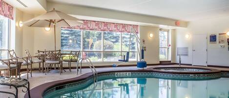 Una piscina interior con zona de estar, sillas y vistas al exterior.