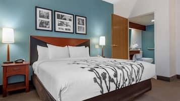 Habitación de hotel con una cama grande, dos mesitas de noche, una mesilla auxiliar, un cabecero de madera y un baño visible a través de una puerta abierta.