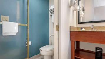 A bathroom with a glass-enclosed shower, a white toilet, a sink with a mirror, and a shelf with toiletries.