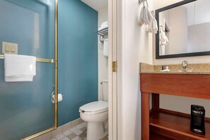 A bathroom with a glass-enclosed shower, a white toilet, a sink with a mirror, and a shelf with toiletries.