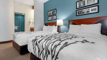 A hotel room with two beds, a blue accent wall, framed pictures, and a wooden headboard.