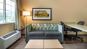 A room with a sofa, a desk, a chair, a lamp, and a picture on the wall.